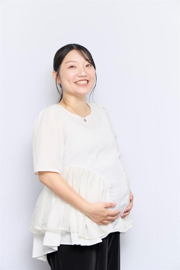 お腹に両手を添えて笑顔を見せる妊婦さん